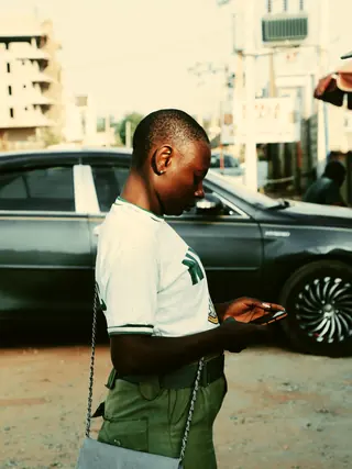 A young person reading a message on their phone in a street in Abuja.