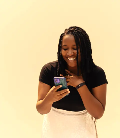A young woman smiling as she looks at her phone.