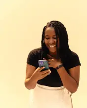 Une jeune femme sourit en regardant son téléphone.