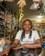 Une commerçante souriante au comptoir de sa boutique, son téléphone posé devant elle.