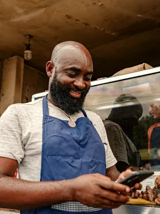A street-food vendor in an apron smiling at his phone.
