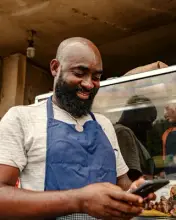 Un vendeur de rue en tablier sourit en regardant son téléphone.